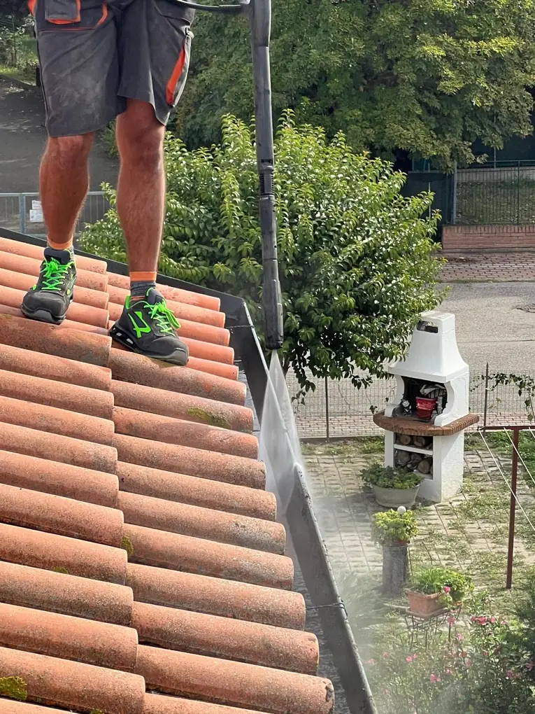 Pulizia della grondaia con lancia ad acqua su tetto in coppi