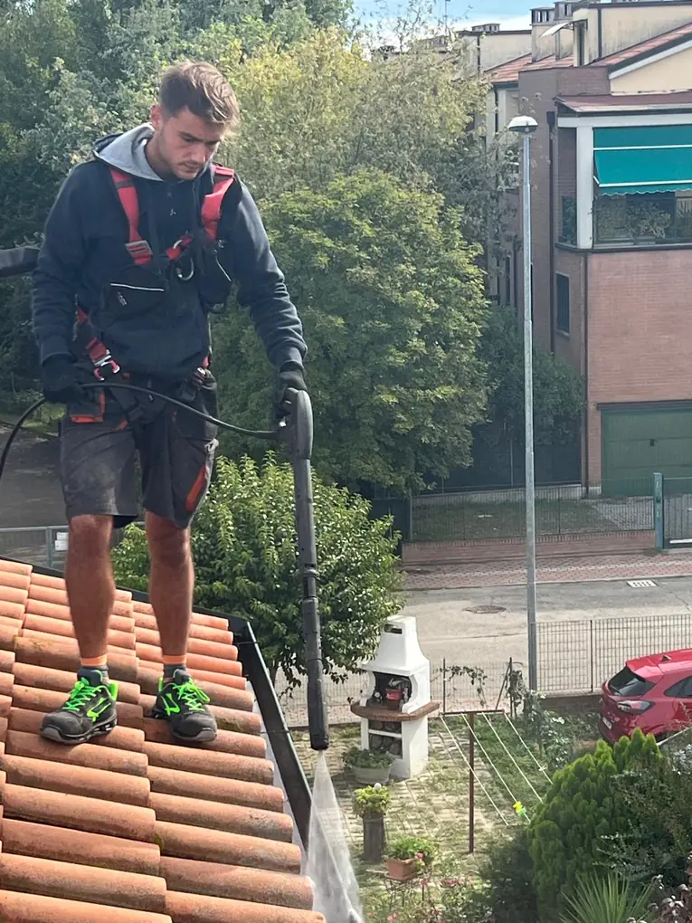 Operatore con imbracatura anticaduta durante la pulizia di tetto e grondaie